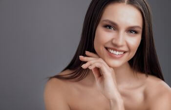 A youthful face of a happy brunette woman with long hair leaning her chin on her hand.